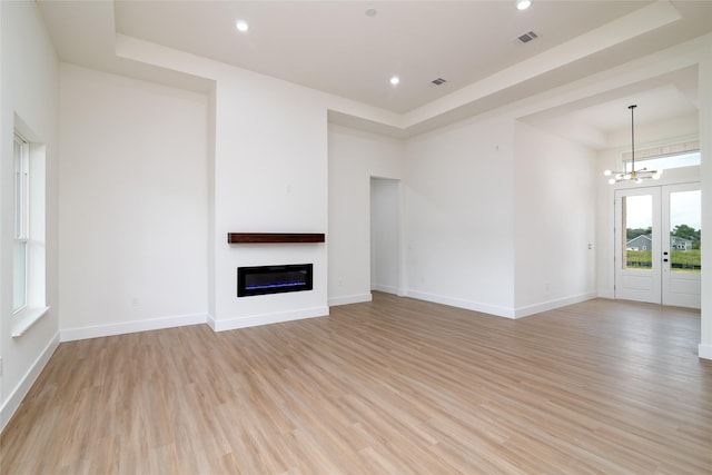 unfurnished living room featuring a chandelier, a raised ceiling, and light hardwood / wood-style flooring