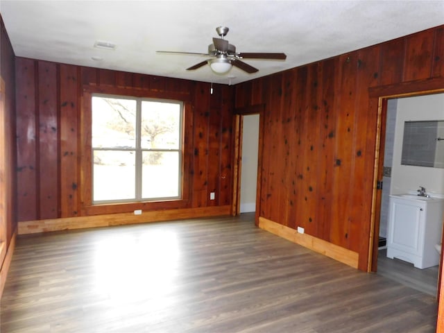 spare room featuring ceiling fan, dark hardwood / wood-style flooring, and wood walls