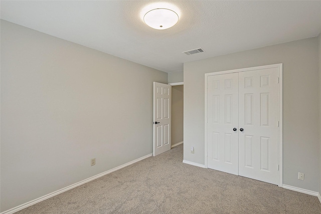 unfurnished bedroom with light carpet, a textured ceiling, and a closet