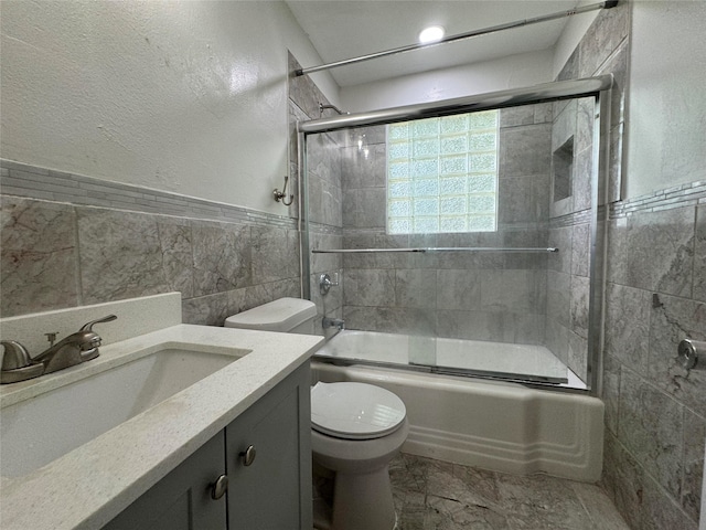 full bathroom featuring toilet, vanity, bath / shower combo with glass door, and tile walls