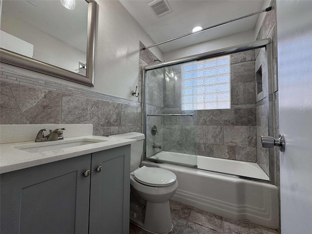 full bath featuring visible vents, toilet, vanity, shower / bath combination with glass door, and tile walls