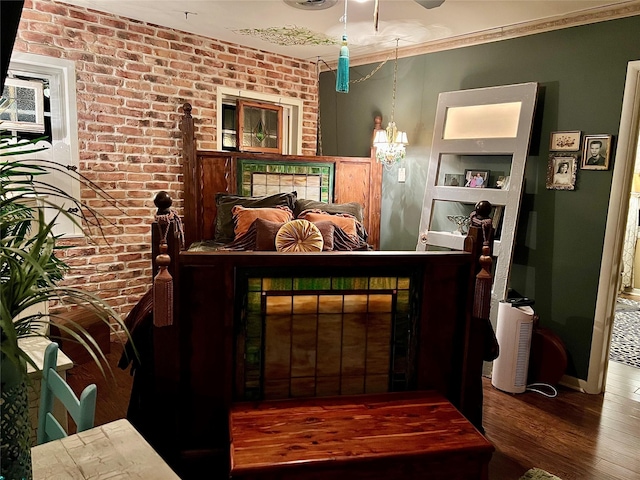 bedroom with a notable chandelier, brick wall, ornamental molding, and hardwood / wood-style flooring