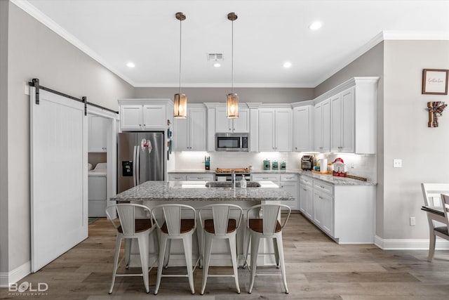 kitchen featuring pendant lighting, a barn door, stainless steel appliances, and light stone counters