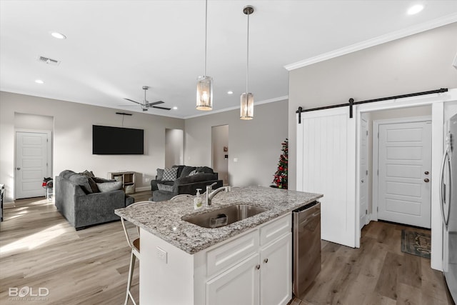 kitchen with stainless steel dishwasher, a kitchen island with sink, sink, a barn door, and white cabinetry