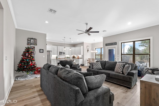 living room with ceiling fan with notable chandelier, crown molding, and light hardwood / wood-style flooring