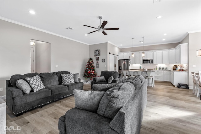 living room with ceiling fan, ornamental molding, a barn door, and light hardwood / wood-style flooring