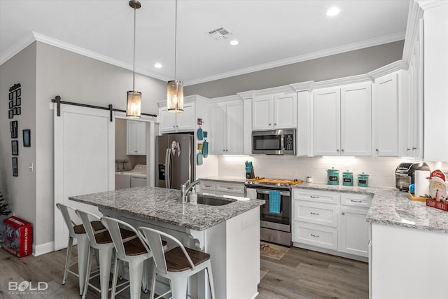 kitchen with sink, appliances with stainless steel finishes, washing machine and dryer, an island with sink, and white cabinets