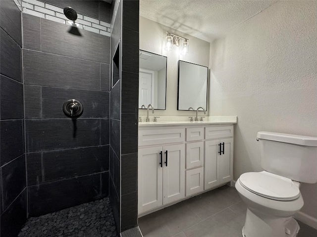 bathroom featuring vanity, tile patterned floors, toilet, a textured ceiling, and a tile shower