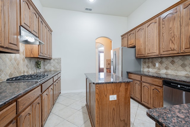 kitchen with decorative backsplash, stainless steel appliances, a kitchen island, and dark stone counters