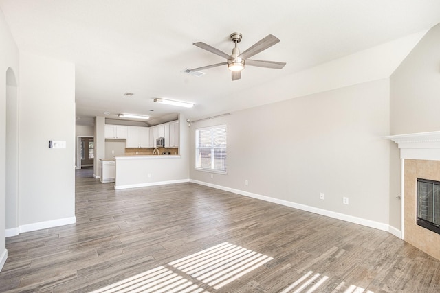 unfurnished living room featuring ceiling fan, a fireplace, and wood-type flooring