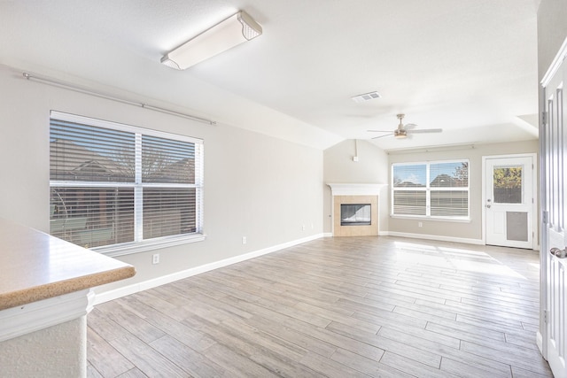 unfurnished living room featuring a tiled fireplace, ceiling fan, lofted ceiling, and light wood-type flooring