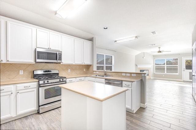 kitchen featuring appliances with stainless steel finishes, backsplash, a healthy amount of sunlight, white cabinets, and a center island