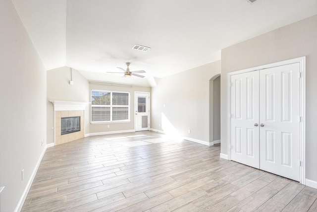 unfurnished living room with a tiled fireplace, ceiling fan, vaulted ceiling, and light wood-type flooring