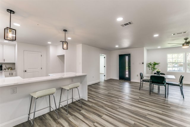 kitchen with ceiling fan, decorative light fixtures, light hardwood / wood-style floors, a kitchen bar, and white cabinetry