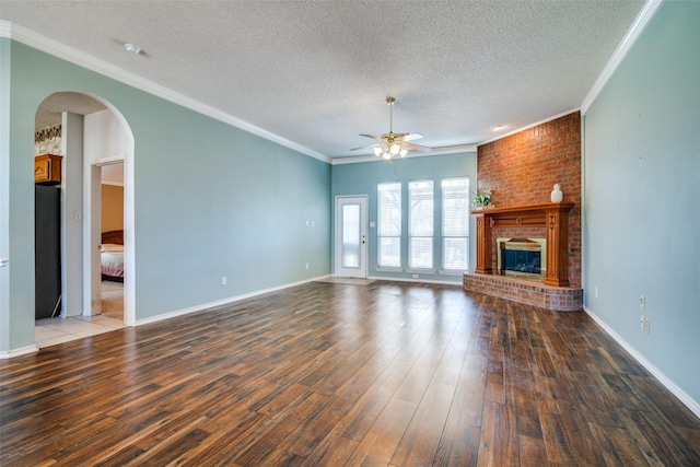 unfurnished living room featuring dark wood-type flooring, crown molding, a brick fireplace, ceiling fan, and a textured ceiling