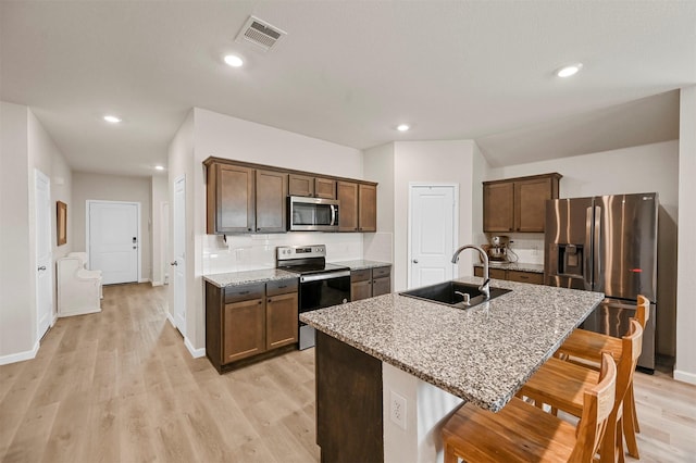 kitchen featuring sink, backsplash, a breakfast bar area, a kitchen island with sink, and appliances with stainless steel finishes