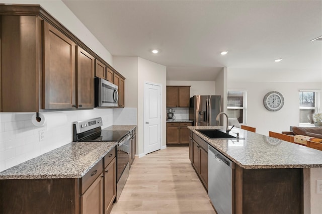 kitchen with appliances with stainless steel finishes, backsplash, light stone counters, and sink