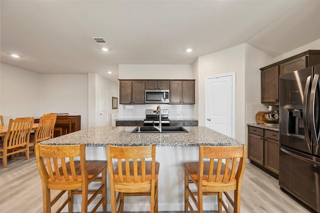 kitchen with light stone countertops, appliances with stainless steel finishes, tasteful backsplash, sink, and an island with sink