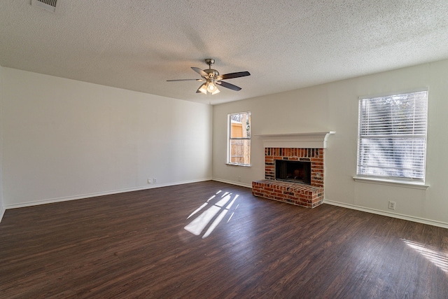 unfurnished living room featuring a brick fireplace, a wealth of natural light, dark wood-type flooring, and ceiling fan