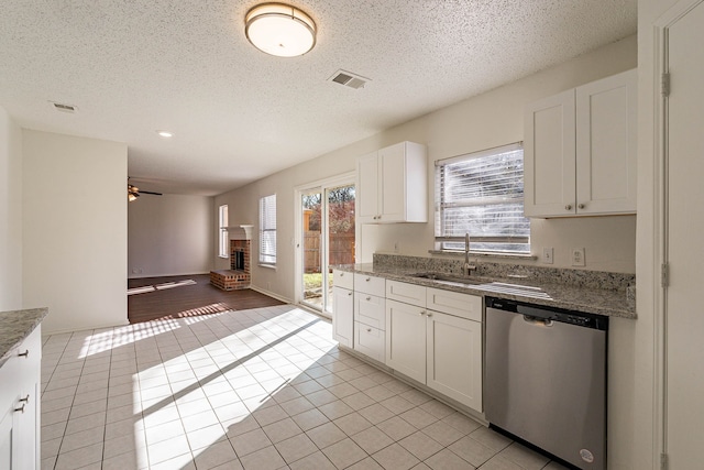 kitchen with a fireplace, dishwasher, sink, white cabinets, and light tile patterned floors