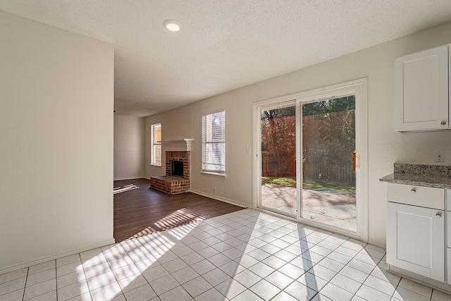 unfurnished living room with light tile patterned flooring, a brick fireplace, and a textured ceiling