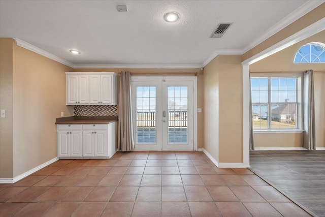 kitchen featuring white cabinets, decorative backsplash, ornamental molding, light tile patterned floors, and french doors