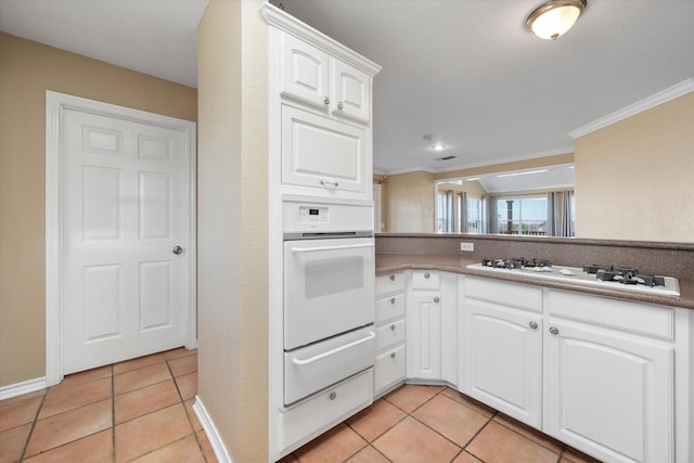 kitchen featuring white appliances, ornamental molding, white cabinets, and light tile patterned flooring