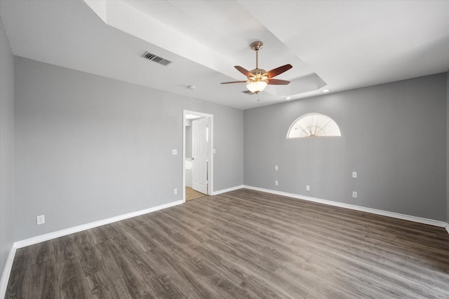 spare room with a tray ceiling, dark wood-type flooring, and ceiling fan