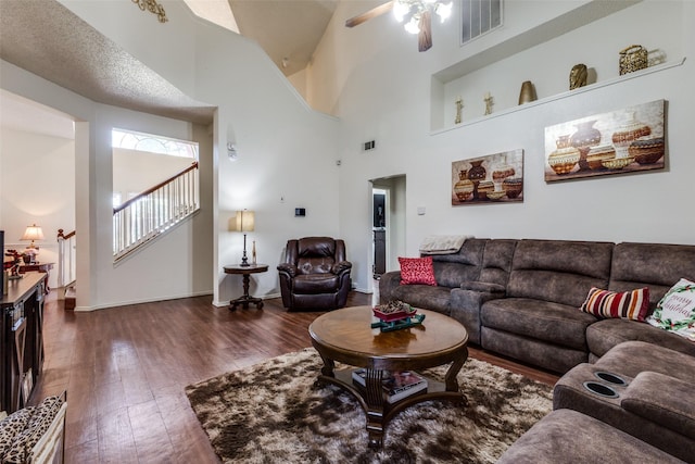 living room with stairs, dark wood-type flooring, visible vents, and a towering ceiling