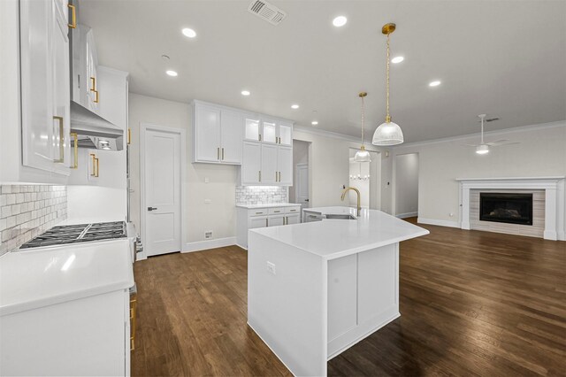 kitchen with pendant lighting, backsplash, white cabinetry, and an island with sink