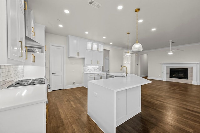 kitchen featuring dark wood-type flooring, wall chimney exhaust hood, a center island with sink, and white cabinets