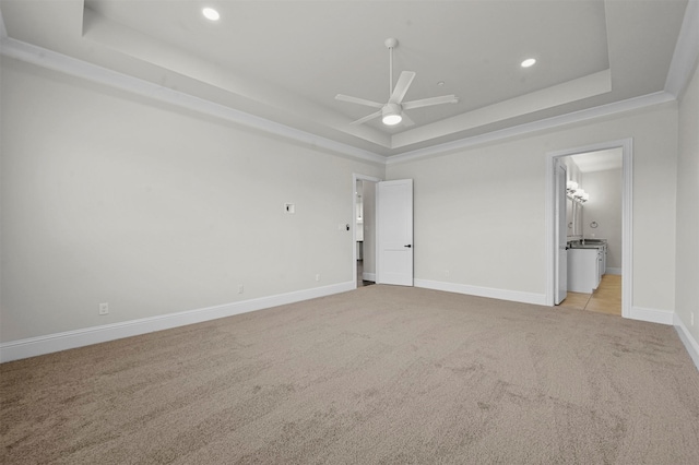 unfurnished bedroom with a tray ceiling, connected bathroom, ceiling fan, and light carpet