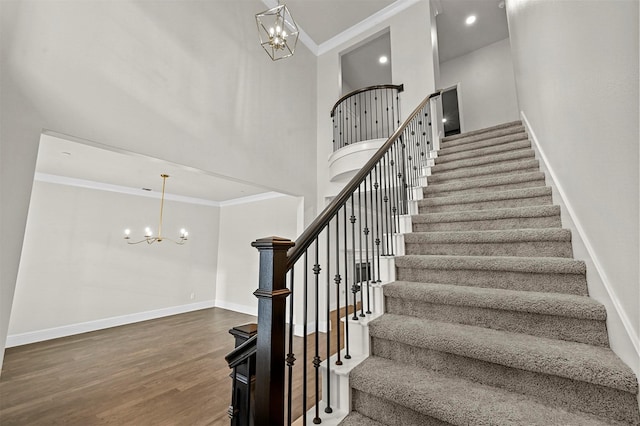 staircase with an inviting chandelier, hardwood / wood-style floors, a towering ceiling, and ornamental molding