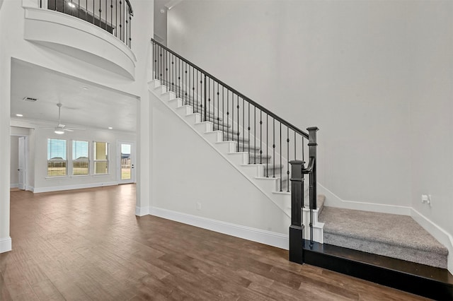 stairway with hardwood / wood-style flooring, ceiling fan, crown molding, and a high ceiling