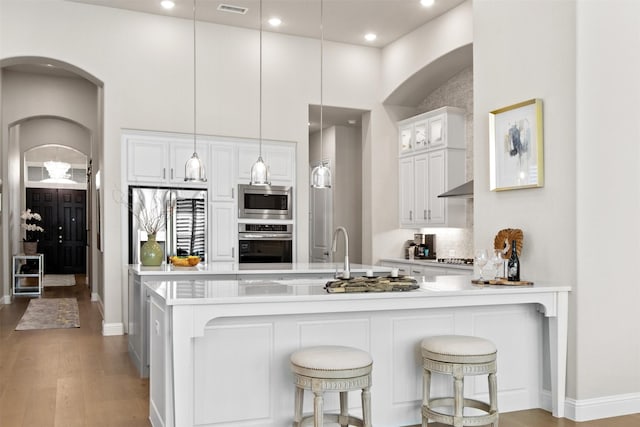 kitchen featuring decorative light fixtures, kitchen peninsula, stainless steel appliances, light hardwood / wood-style floors, and white cabinets