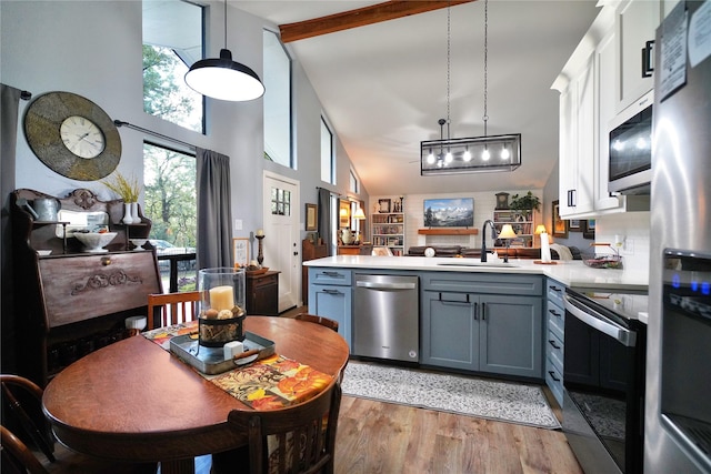 kitchen with sink, stainless steel appliances, beamed ceiling, kitchen peninsula, and white cabinets