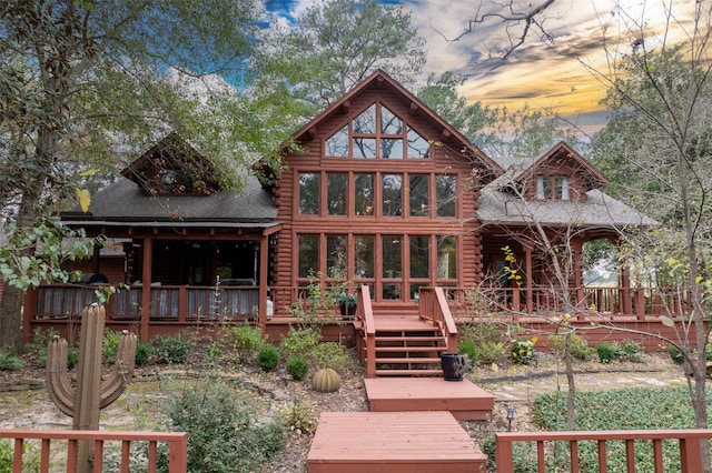 back house at dusk featuring a wooden deck and a sunroom