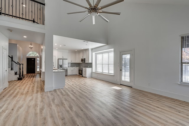 unfurnished living room featuring a towering ceiling, ceiling fan with notable chandelier, and light wood-type flooring