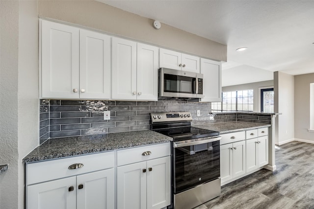 kitchen featuring dark wood-type flooring, backsplash, dark stone countertops, white cabinets, and appliances with stainless steel finishes