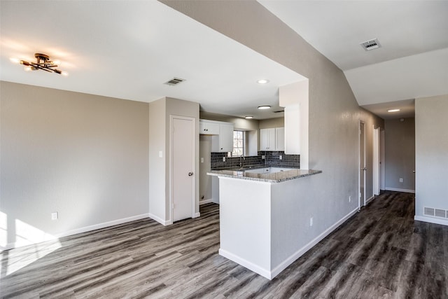 kitchen featuring white cabinets, decorative backsplash, dark hardwood / wood-style floors, light stone counters, and kitchen peninsula