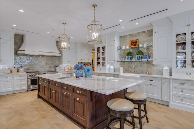 kitchen featuring stainless steel stove, sink, backsplash, custom exhaust hood, and a kitchen island with sink