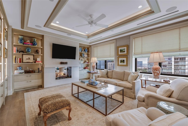 living room featuring built in shelves, a multi sided fireplace, a tray ceiling, and light wood-type flooring