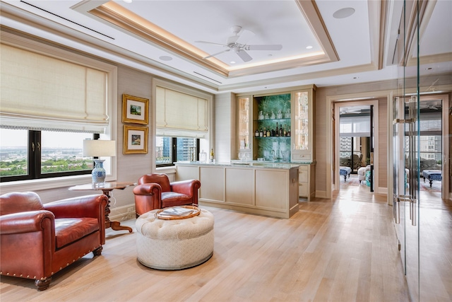 sitting room with ceiling fan, bar, a tray ceiling, and light hardwood / wood-style flooring