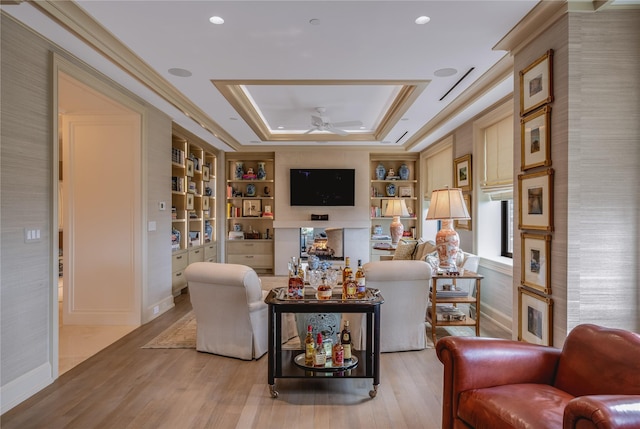 living room featuring light hardwood / wood-style flooring, ceiling fan, ornamental molding, built in shelves, and a raised ceiling