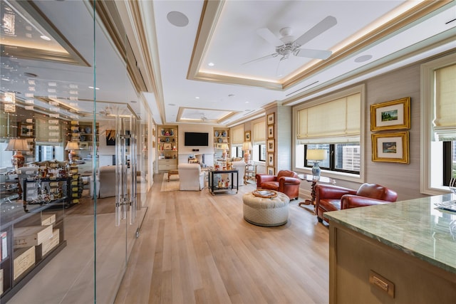 living room with crown molding, ceiling fan, wood-type flooring, and a tray ceiling