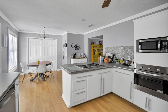 kitchen with appliances with stainless steel finishes, ornamental molding, light hardwood / wood-style floors, white cabinets, and kitchen peninsula