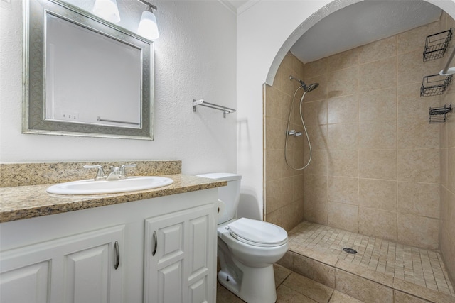 bathroom featuring tile patterned flooring, a tile shower, vanity, and toilet