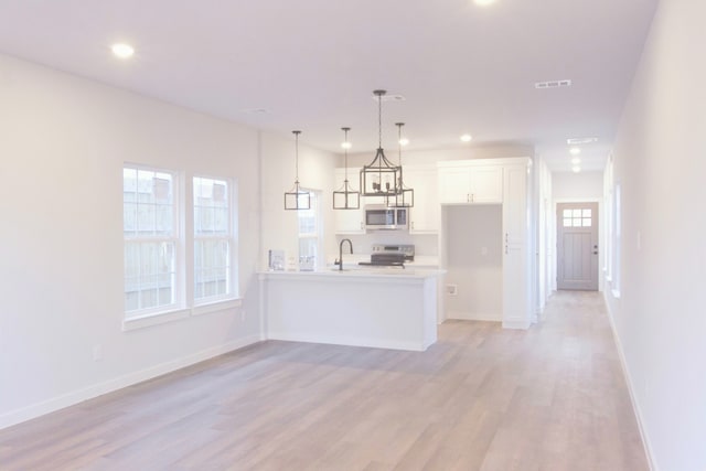 kitchen with pendant lighting, white cabinetry, stainless steel appliances, sink, and light hardwood / wood-style flooring