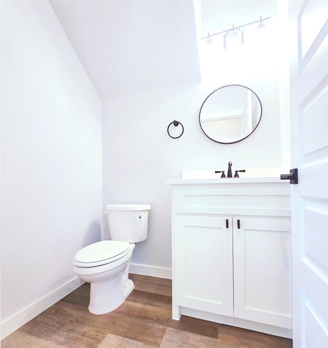 bathroom featuring wood-type flooring, toilet, vanity, and vaulted ceiling