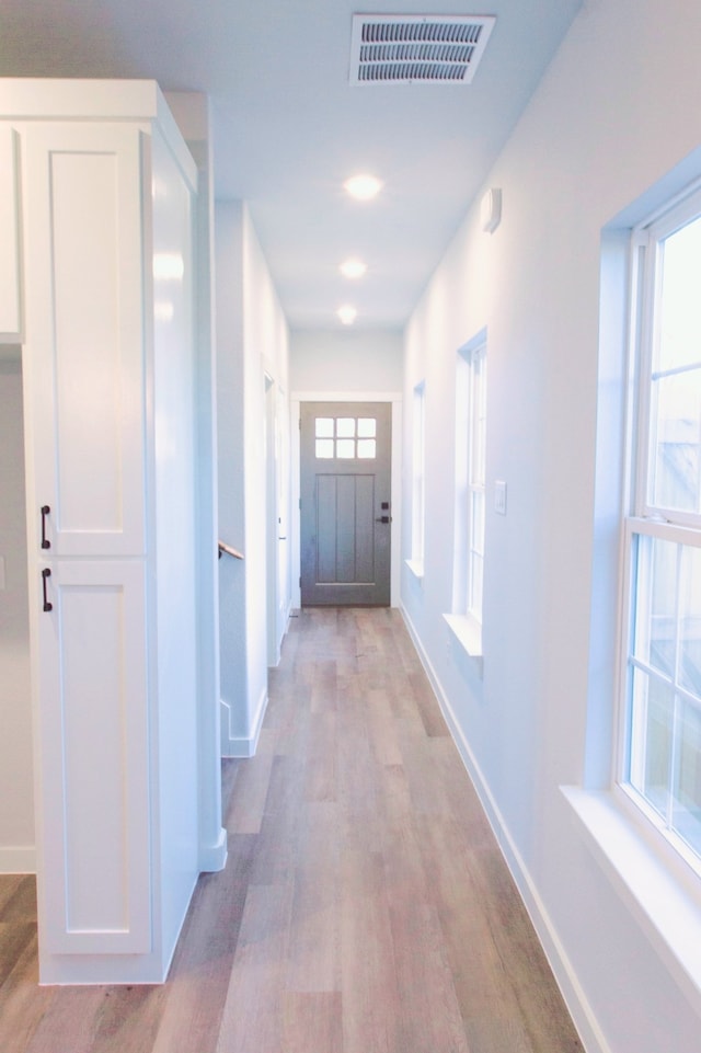 hallway with a healthy amount of sunlight and light hardwood / wood-style floors